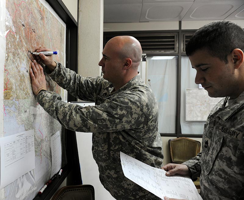 One Soldier marking a wall map with another and another Soldier reading a document