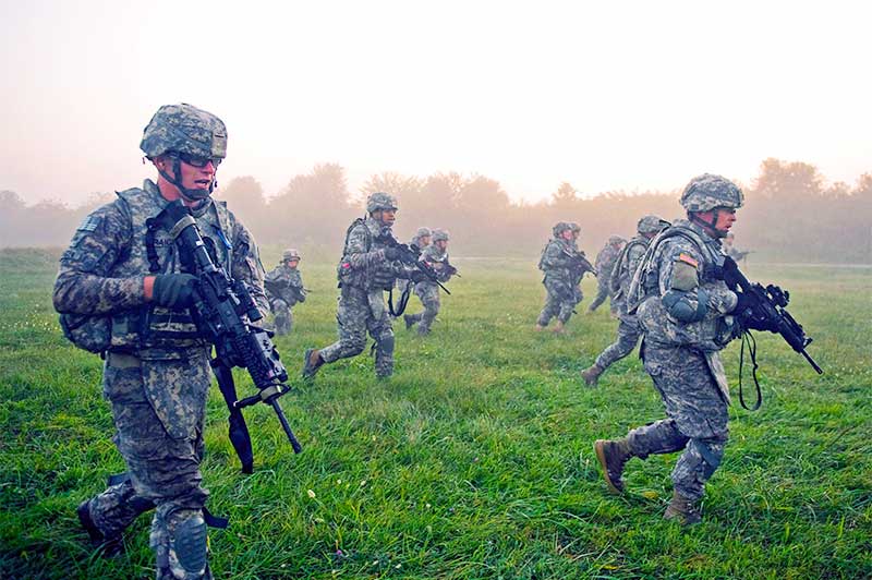 Soldiers running in an open grassy area holding guns