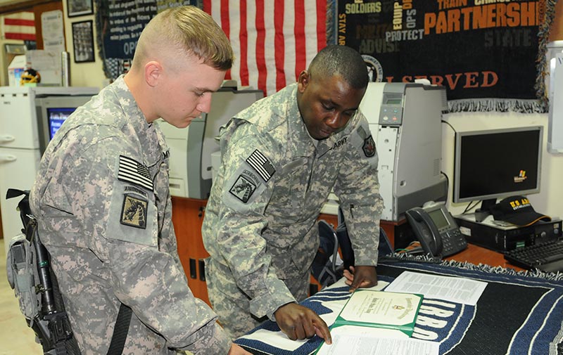 Two Soldiers stand before a desk looking at paperwork