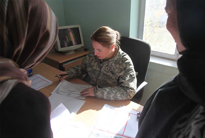 A major writes at a desk while two women watch